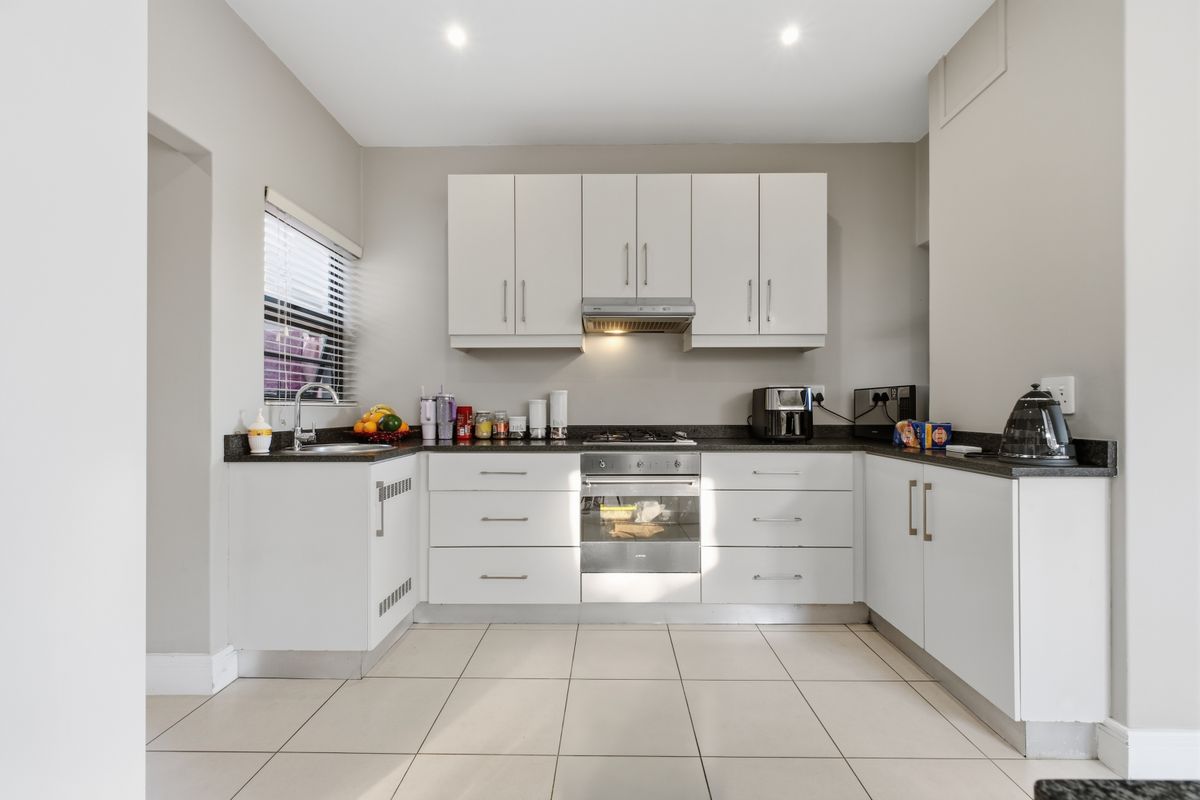 A clean and functional kitchen featuring white cabinetry, dark countertops, a gas hob, built-in oven, and tiled flooring.