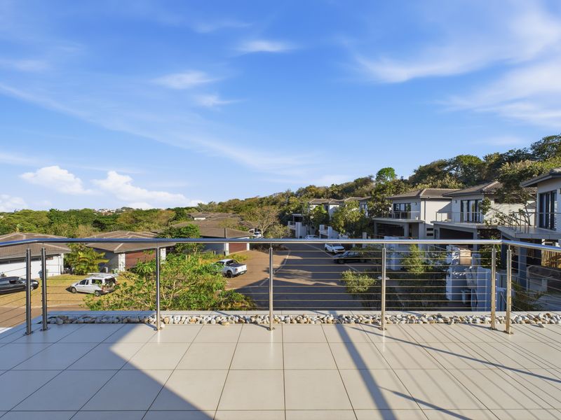 Spacious elevated balcony featuring modern tiled flooring and a stainless steel balustrade, offering expansive views of the surrounding residential estate.