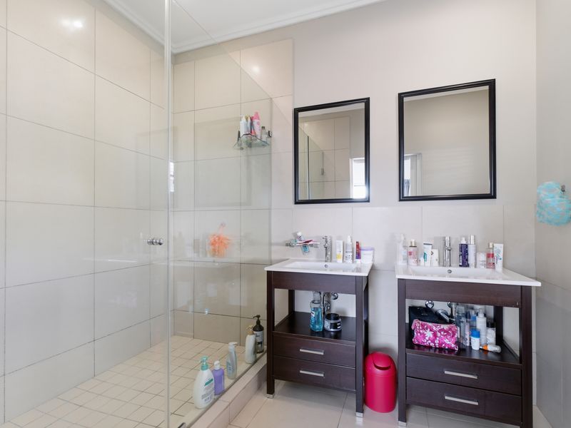A modern bathroom featuring a double vanity with dark wood cabinetry, wall-mounted mirrors, and a spacious walk-in shower with a glass enclosure.