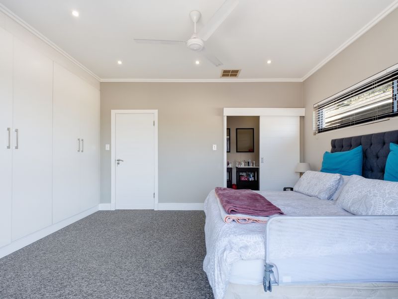 Spacious bedroom featuring neutral walls, plush carpeting, extensive built-in cabinetry, a ceiling fan, and direct access to an en-suite bathroom.