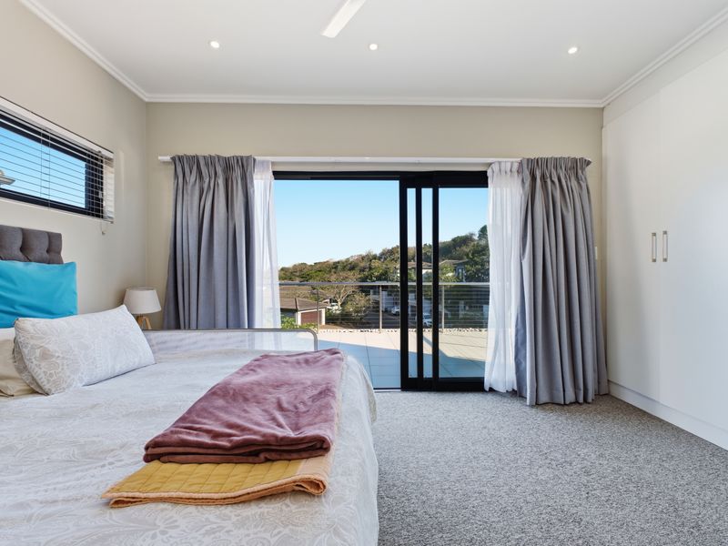 Spacious bedroom featuring built-in wardrobes, carpet flooring, and sliding glass doors opening onto a private balcony with scenic views.