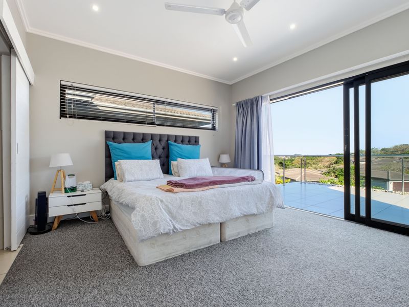 Spacious bedroom featuring neutral carpeting, a ceiling fan, and large sliding glass doors opening onto a private balcony with scenic views.