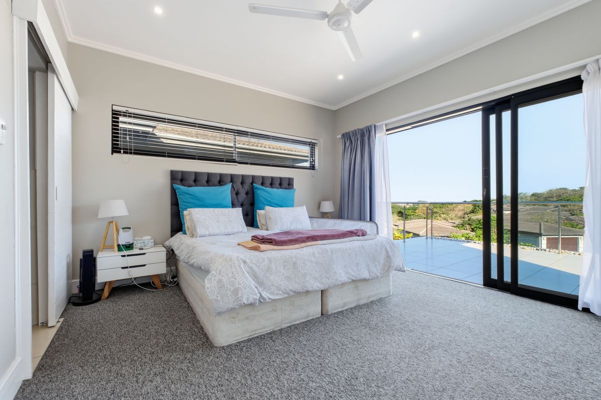Spacious bedroom featuring neutral carpeting, a ceiling fan, and large sliding glass doors opening onto a private balcony with scenic views.