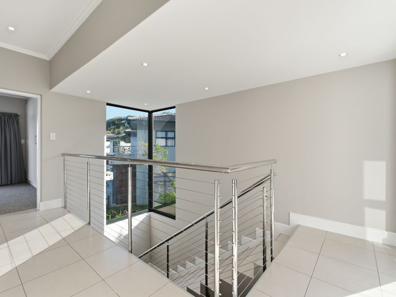 A bright and modern landing area featuring sleek stainless steel and wire cable balustrades, tiled flooring, and a large corner window overlooking the exterior.