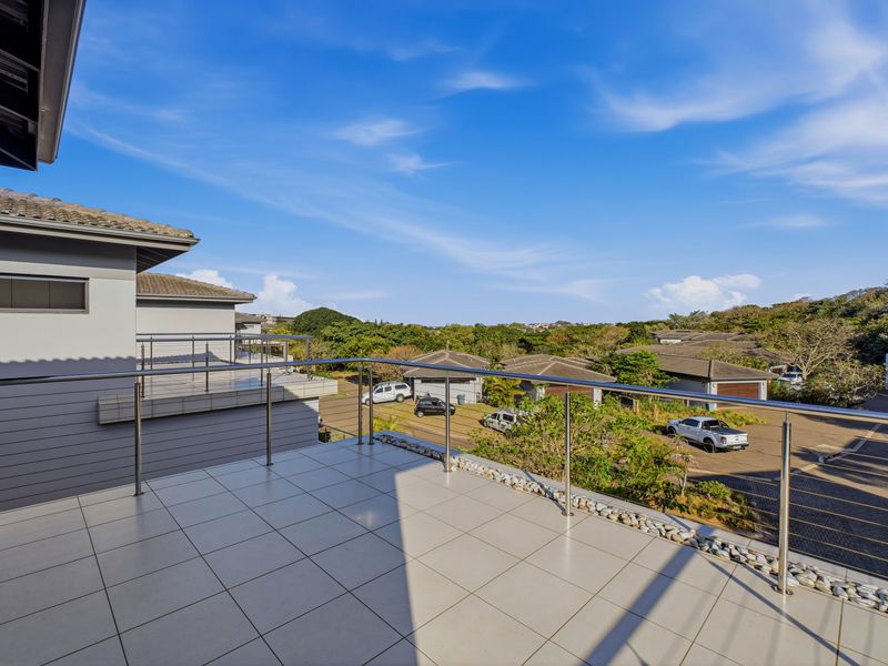 A spacious, well-maintained balcony featuring modern stainless steel balustrades, tiled flooring, and a pebble drainage border, offering elevated views of the surrounding estate.