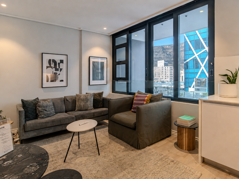 A bright, modern living room featuring large windows with city and mountain views, recessed lighting, and neutral finishes.