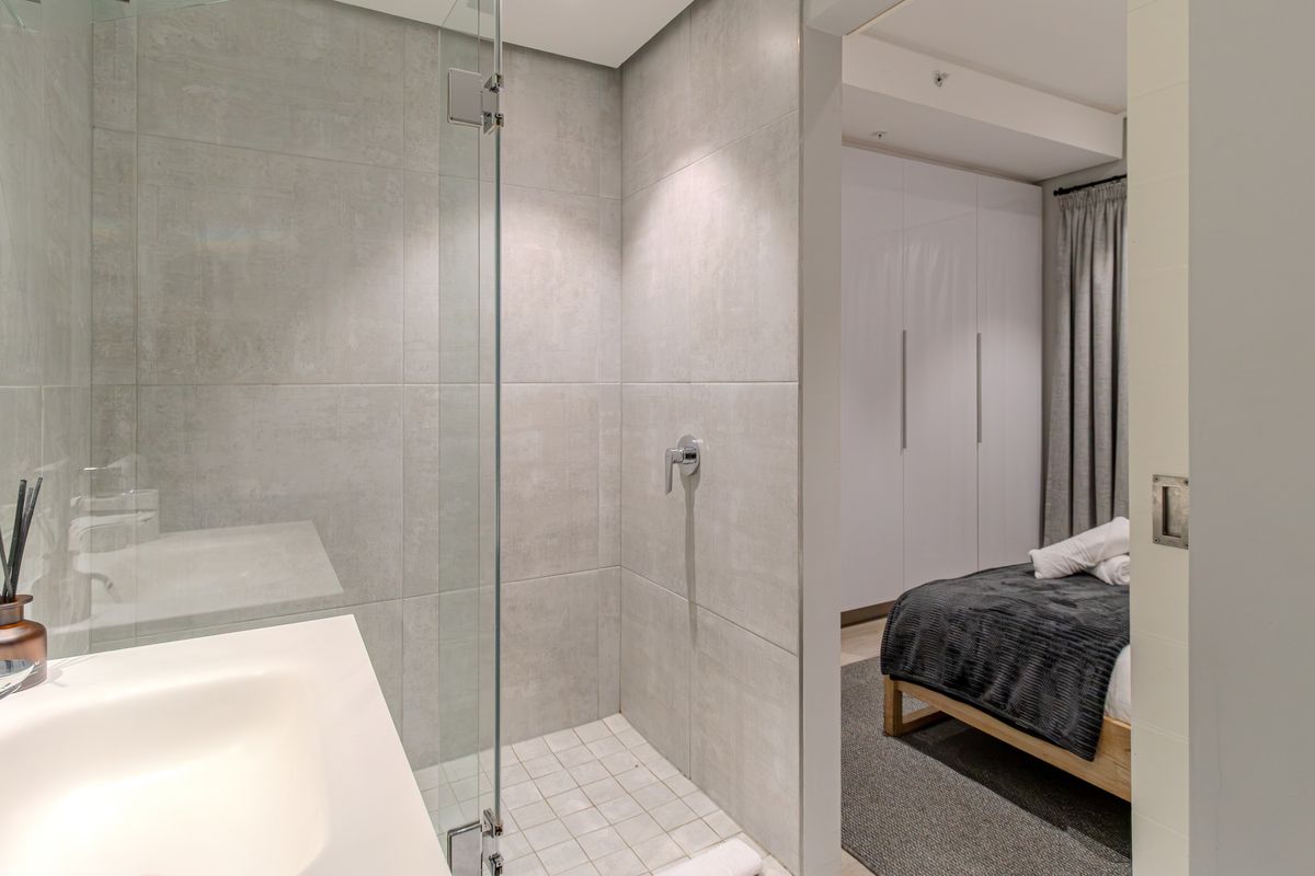 Modern bathroom featuring a glass-enclosed shower with neutral tiling, adjacent to a bedroom with built-in wardrobe storage.