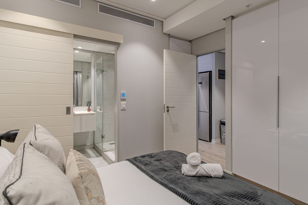 Modern bedroom featuring a built-in wardrobe, ducted air conditioning, and direct access to a sleek en-suite bathroom with a glass-enclosed shower.