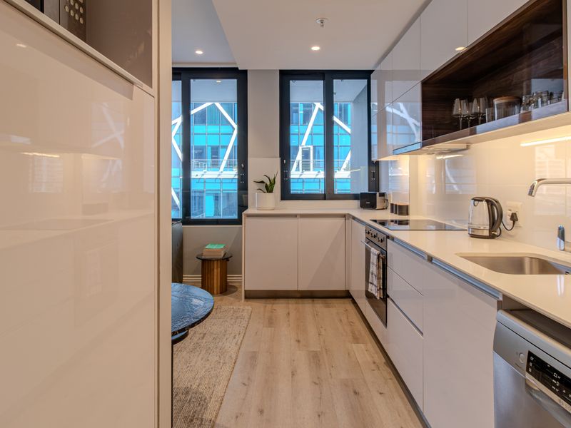 Modern galley-style kitchen featuring sleek white cabinetry, integrated appliances, high-quality finishes, and ample natural light from large windows.