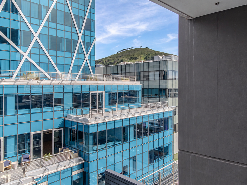 A view from a balcony overlooking modern glass-facade commercial buildings and a distant hill.