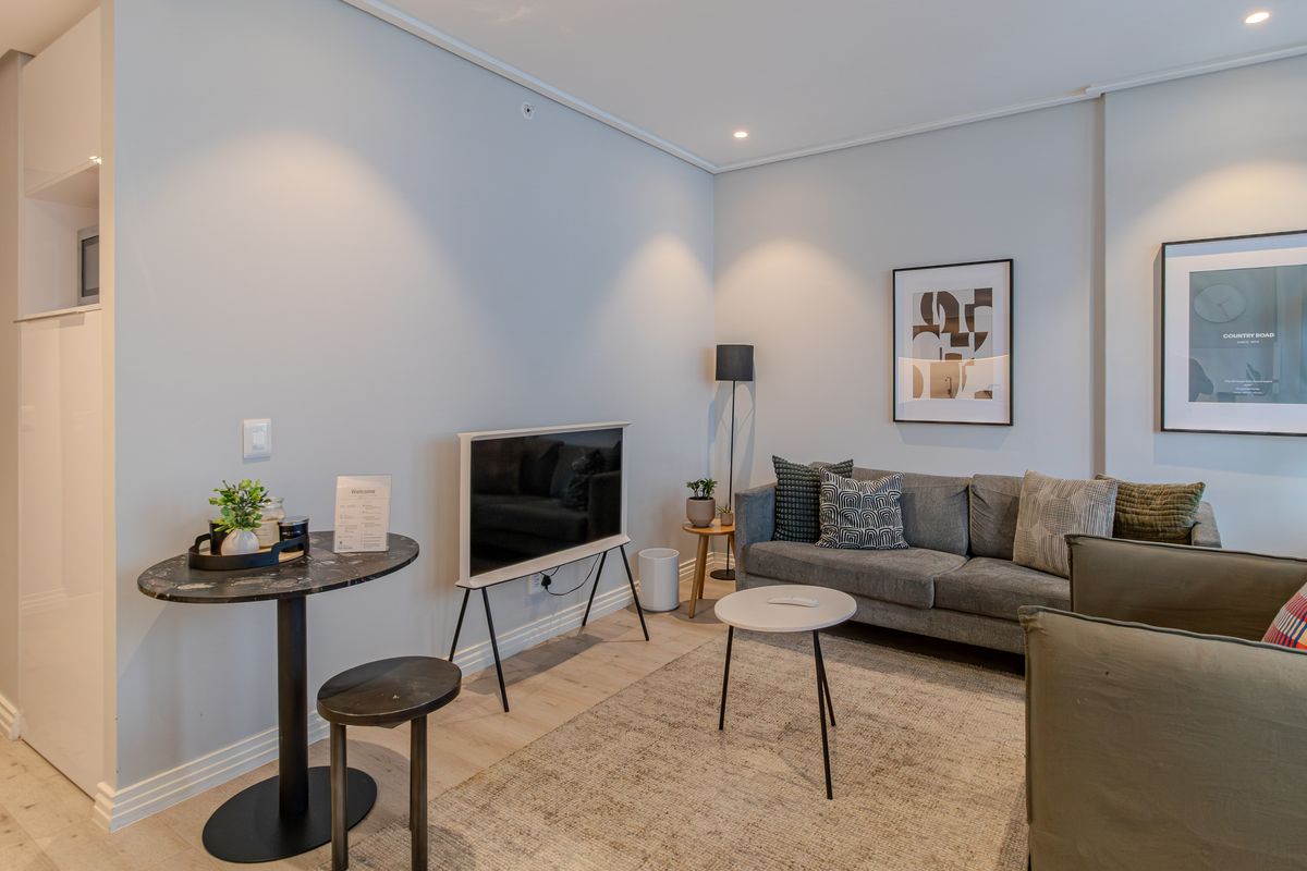 A well-maintained living room featuring modern recessed downlighting, light-toned laminate flooring, and clean wall finishes.