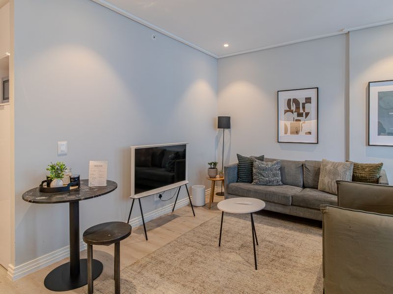 A well-maintained living room featuring modern recessed downlighting, light-toned laminate flooring, and clean wall finishes.