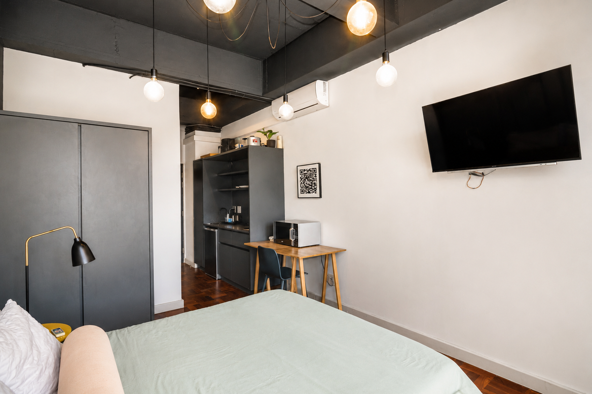 Modern studio bedroom featuring parquet flooring, a built-in wardrobe, split-system air conditioning, and a compact kitchenette area with sink and cabinetry.