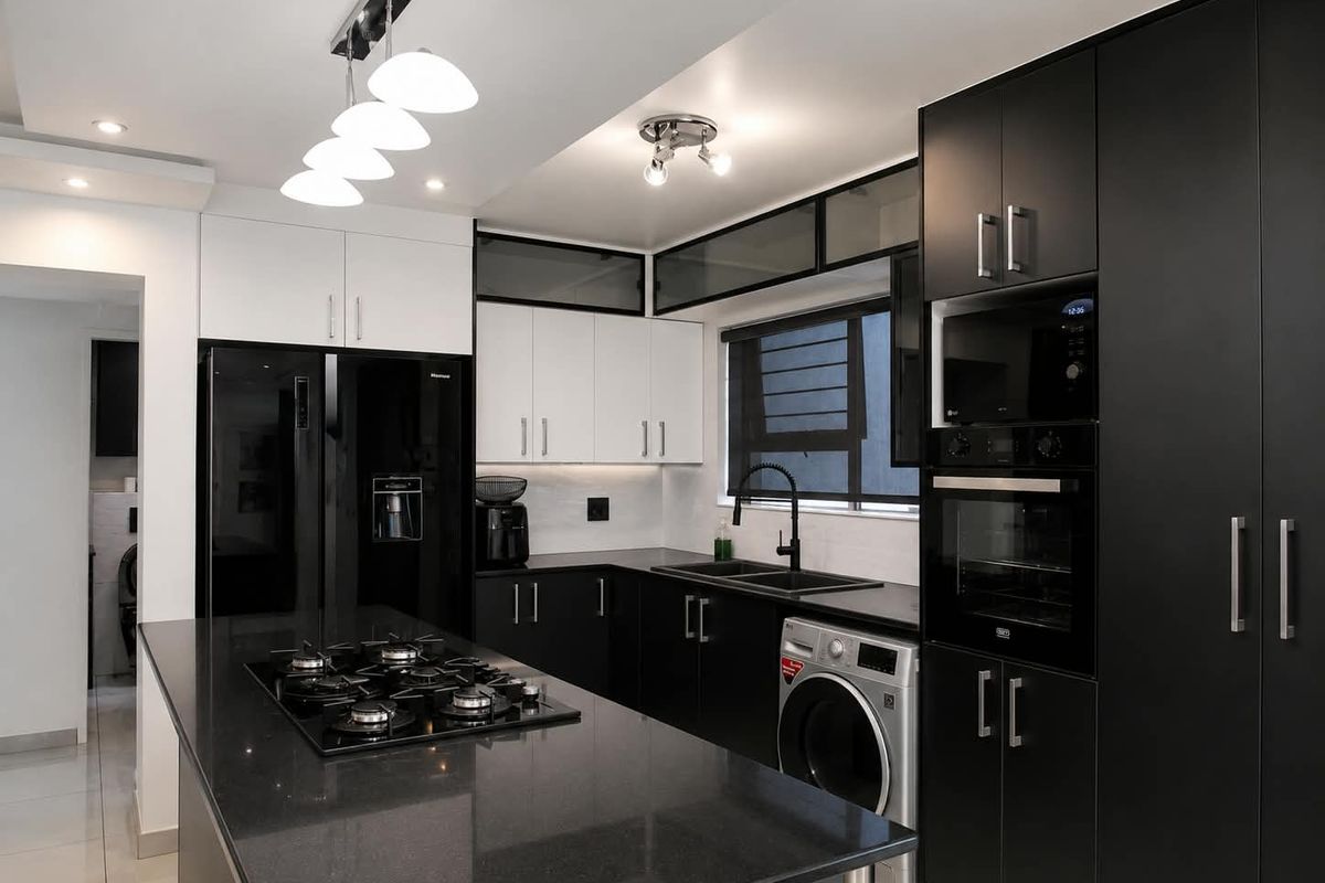 Modern kitchen featuring sleek black and white cabinetry, stone countertops, a gas hob, built-in appliances, and integrated laundry facilities.
