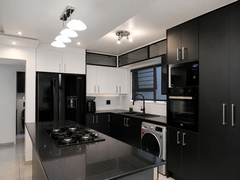 Modern kitchen featuring sleek black and white cabinetry, stone countertops, a gas hob, built-in appliances, and integrated laundry facilities.