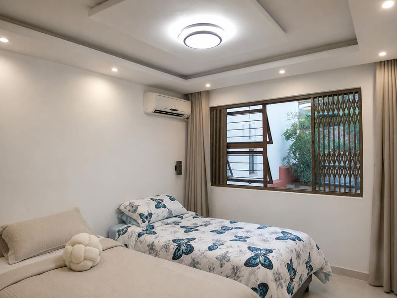 A well-maintained bedroom featuring recessed ceiling lighting, a split-system air conditioner, and a window with integrated security gate.