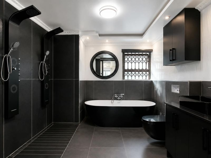 Modern, high-contrast bathroom featuring a sleek freestanding bathtub, dual shower panels, wall-mounted toilet, and contemporary vanity cabinetry with premium finishes.