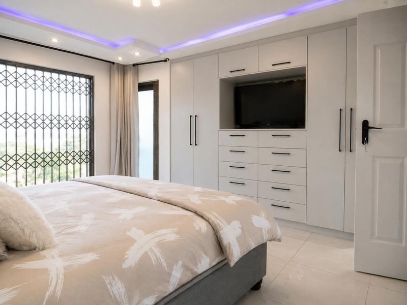 Modern bedroom featuring extensive built-in cabinetry with integrated media storage, tiled flooring, and decorative recessed ceiling lighting with ambient purple accents.
