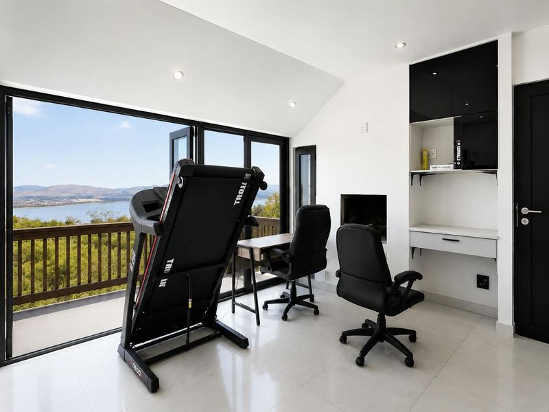 Modern home office featuring built-in cabinetry, a sleek desk, tiled flooring, and large bi-fold doors opening to a scenic balcony view.