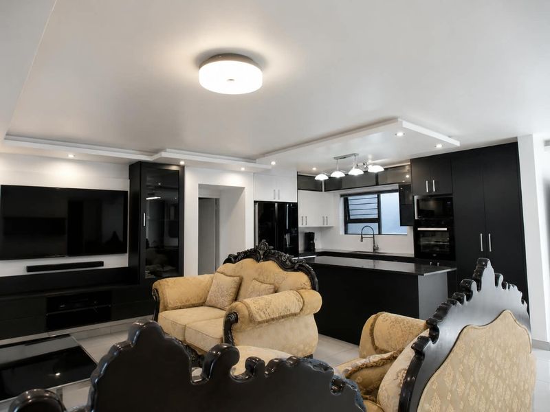 Modern open-plan living area featuring a sleek kitchen with dark cabinetry, a central island, and integrated appliances, seamlessly connected to the living space.