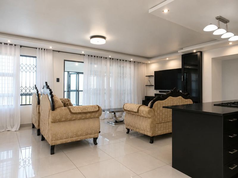 Spacious open-plan living area featuring polished porcelain tiles, recessed ceiling lighting, and a modern kitchen island, seamlessly connecting to the outdoor balcony.