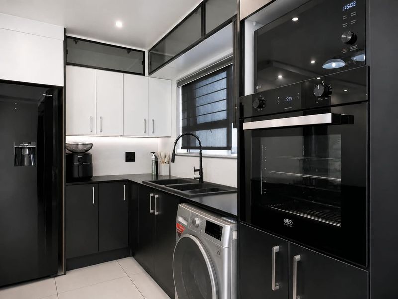 Modern kitchen featuring sleek black and white cabinetry, integrated appliances, black stone countertops, and high-quality finishes in a contemporary design.