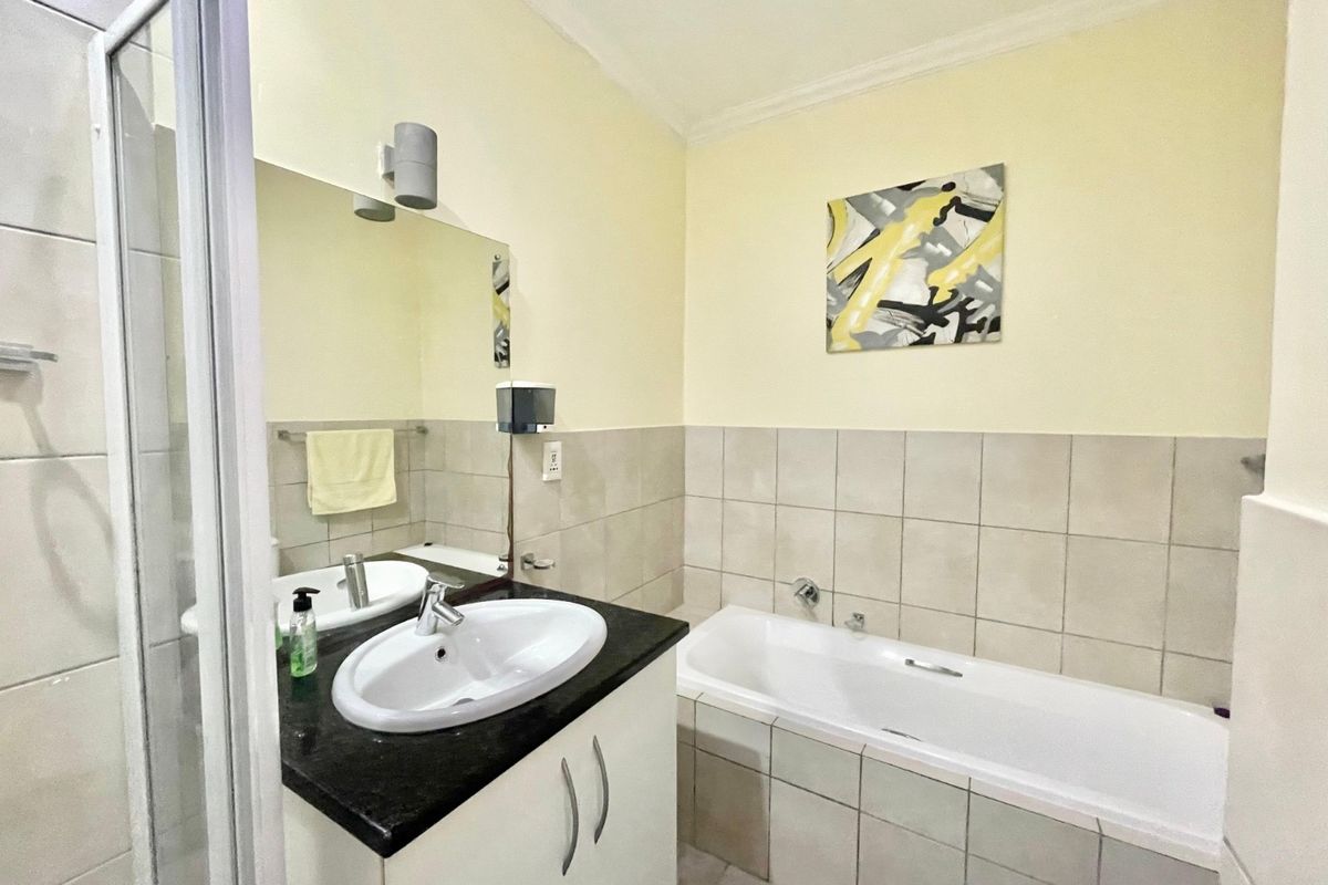 A functional bathroom featuring a vanity with granite countertop, a bathtub, and a separate shower enclosure with neutral wall tiling.
