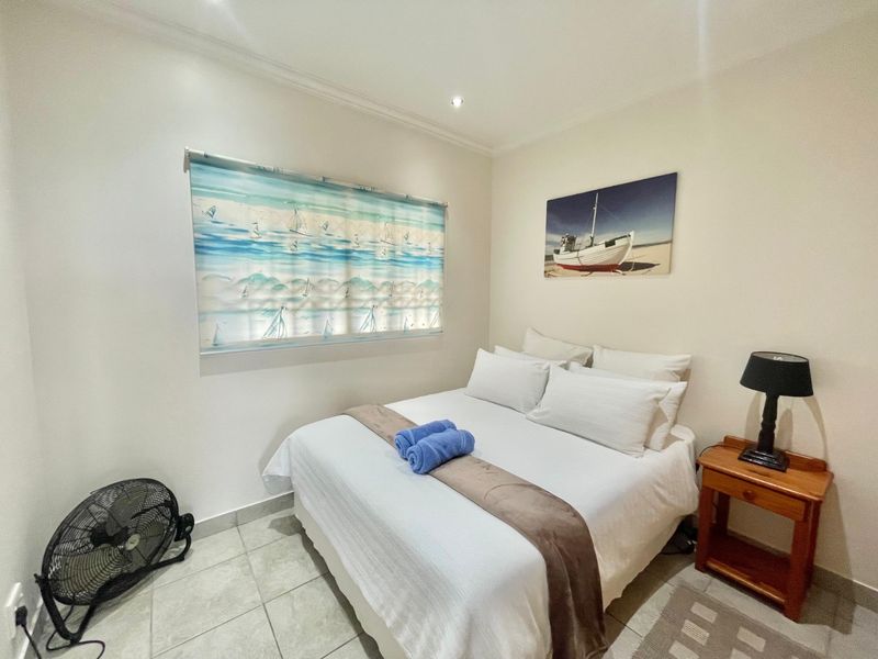 A compact bedroom featuring tiled flooring, recessed downlighting, and a roller blind, providing a functional and neutral sleeping space.