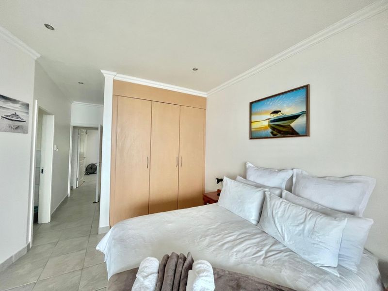 A well-maintained bedroom featuring neutral tiled flooring, recessed downlighting, and a large built-in wooden wardrobe with ample storage space.
