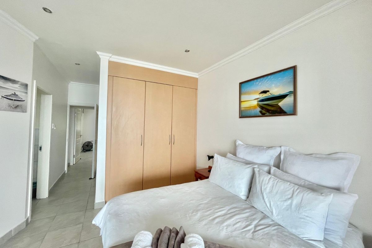 A well-maintained bedroom featuring neutral tiled flooring, recessed downlighting, and a large built-in wooden wardrobe with ample storage space.