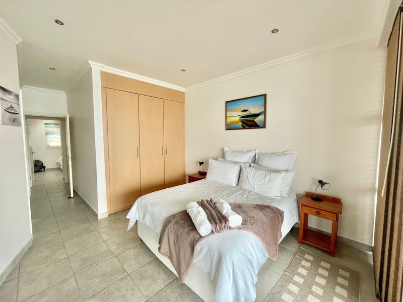 A well-maintained bedroom featuring neutral tiled flooring, recessed downlighting, and ample built-in cupboard storage space.
