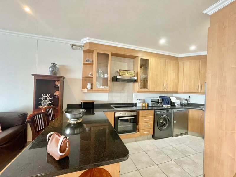 A functional kitchen featuring light wood cabinetry, dark granite countertops, integrated oven and hob, and tiled flooring with recessed lighting.