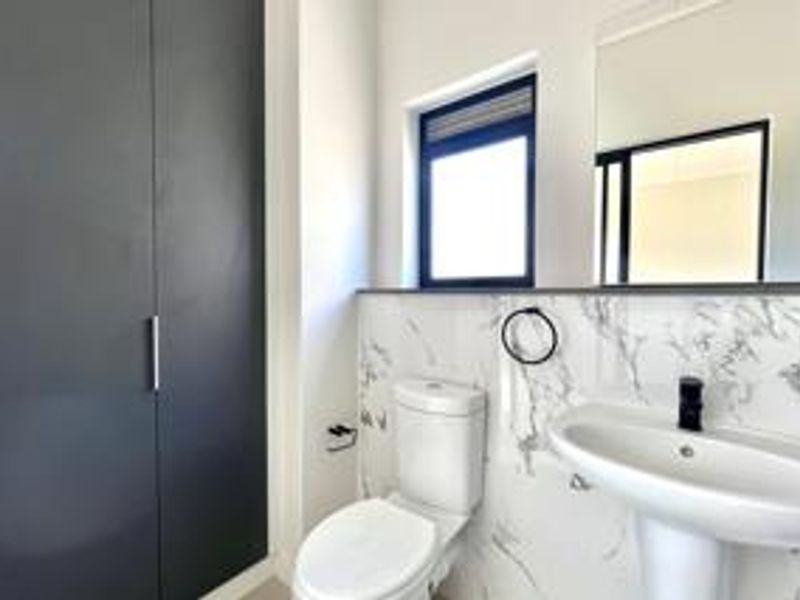 Modern bathroom featuring a pedestal basin, toilet, built-in storage cupboard, and elegant marble-look wall tiling.