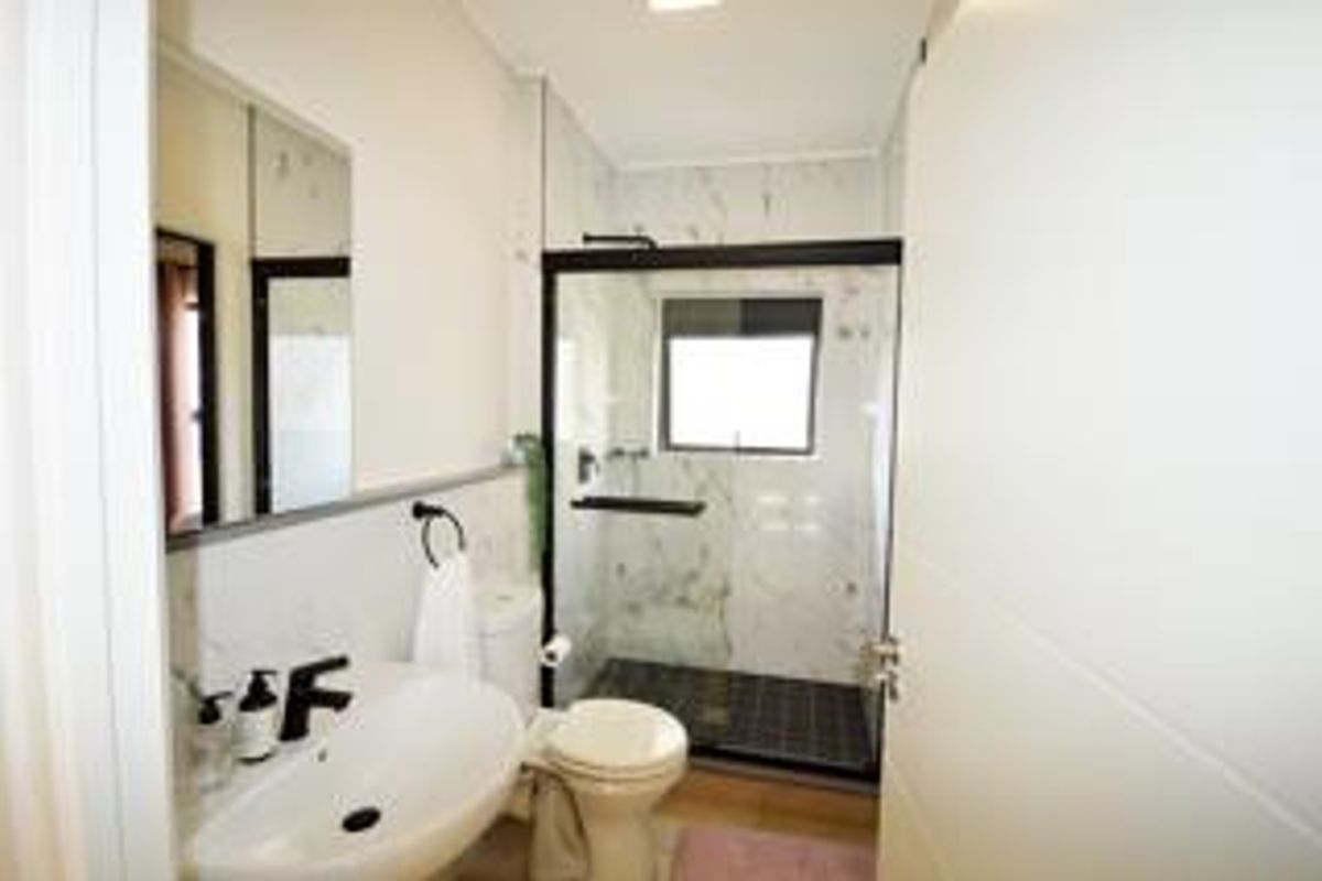 Modern bathroom featuring a walk-in shower with a glass enclosure, marble-look wall tiles, a contemporary basin, and sleek black fixtures.