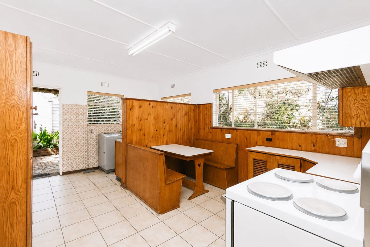A dated kitchen featuring built-in timber booth seating, tiled flooring, and original cabinetry, offering significant potential for a modern renovation.