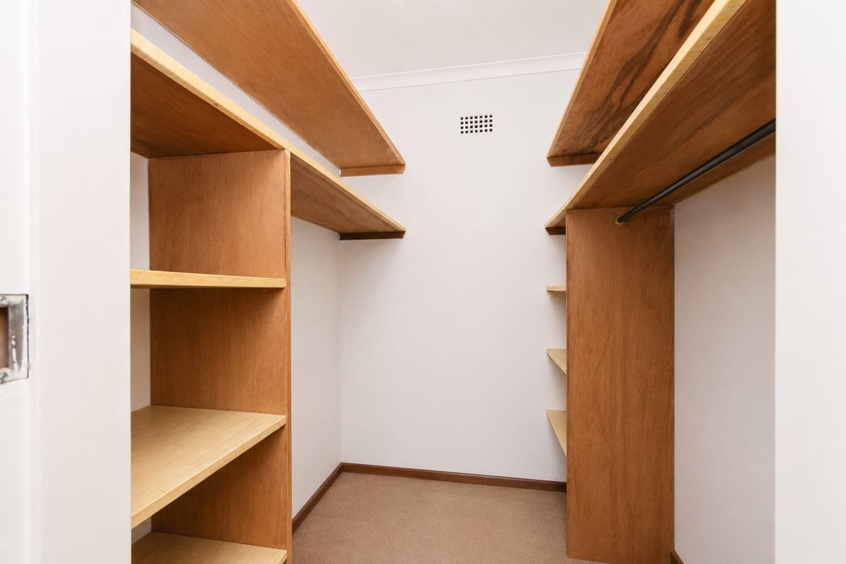 A walk-in wardrobe featuring built-in timber shelving and a hanging rail, providing organized storage space.