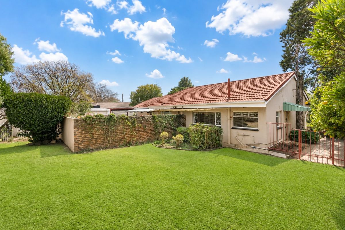 Rear view of the property featuring a well-maintained lawn, a brick boundary wall, and a tiled roof structure.