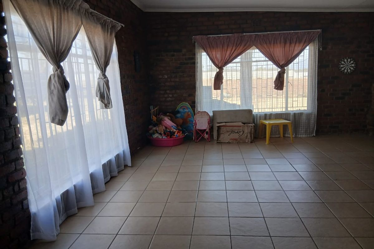 Spacious living area featuring exposed brick walls, large windows with security bars, and neutral ceramic floor tiles.