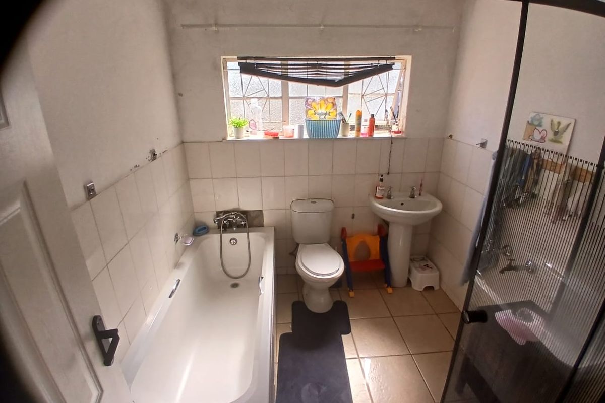 A dated bathroom featuring a bathtub, pedestal basin, and toilet, with tiled finishes and a window with security bars.