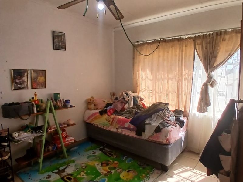 A bedroom featuring tiled flooring and a ceiling fan. The room requires maintenance, particularly regarding the exposed electrical wiring.