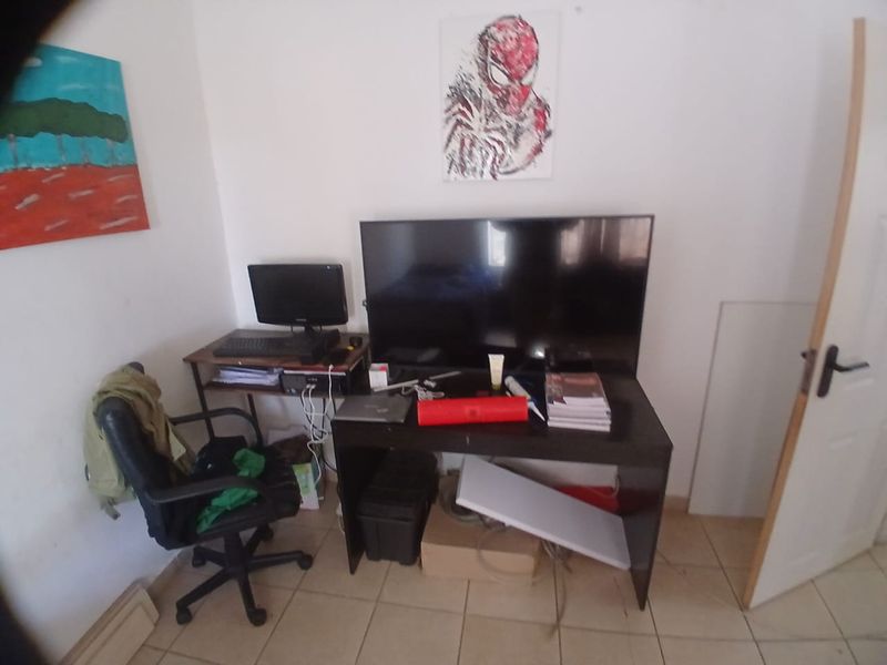 A bedroom space featuring tiled flooring and a standard internal door, currently utilized as a home office and media area.