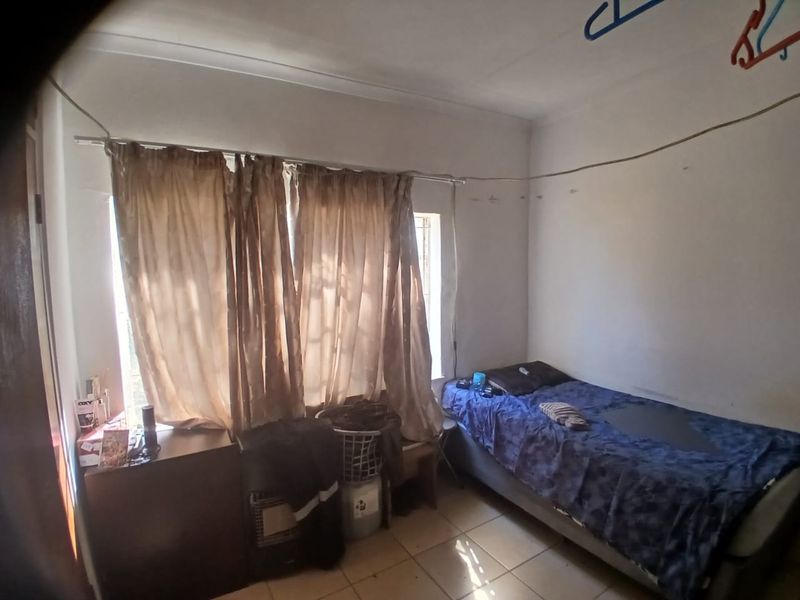 A bedroom featuring tiled flooring and a coved ceiling, currently requiring cosmetic updates to the wall finishes and general maintenance.