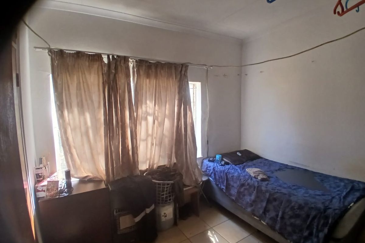 A bedroom featuring tiled flooring and a coved ceiling, currently requiring cosmetic updates to the wall finishes and general maintenance.
