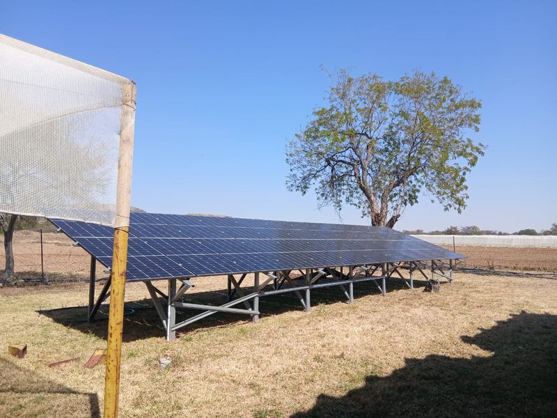 A ground-mounted solar panel array installed on a metal support structure within a garden area.