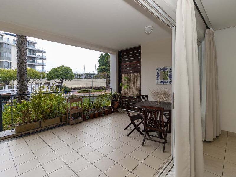 A covered balcony featuring tiled flooring, a metal railing, and a timber privacy screen, offering views of the surrounding marina area.