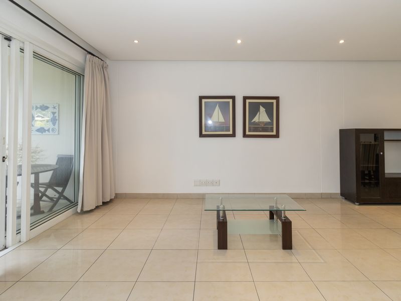 A bright and spacious living area featuring neutral tiled flooring, recessed lighting, and a large sliding glass door providing access to the outdoor patio.