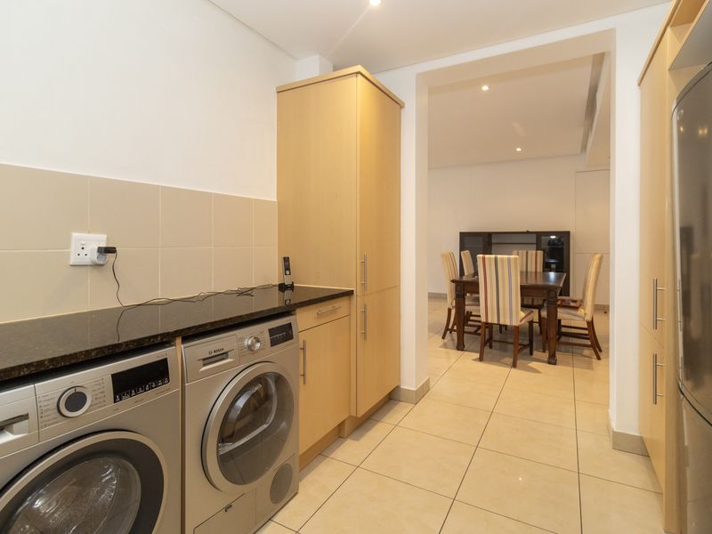 A functional laundry area featuring built-in cabinetry, granite countertops, and tiled finishes, with a seamless transition into the adjacent dining space.