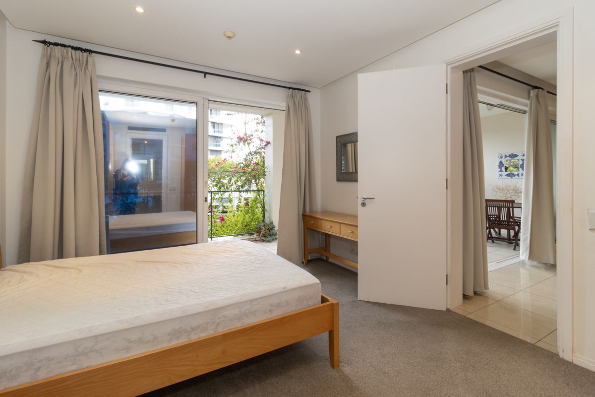 A well-lit bedroom featuring carpeted flooring, recessed downlights, and a sliding glass door providing access to a private balcony.