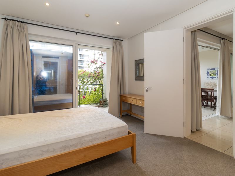 A well-lit bedroom featuring carpeted flooring, recessed downlights, and a sliding glass door providing access to a private balcony.