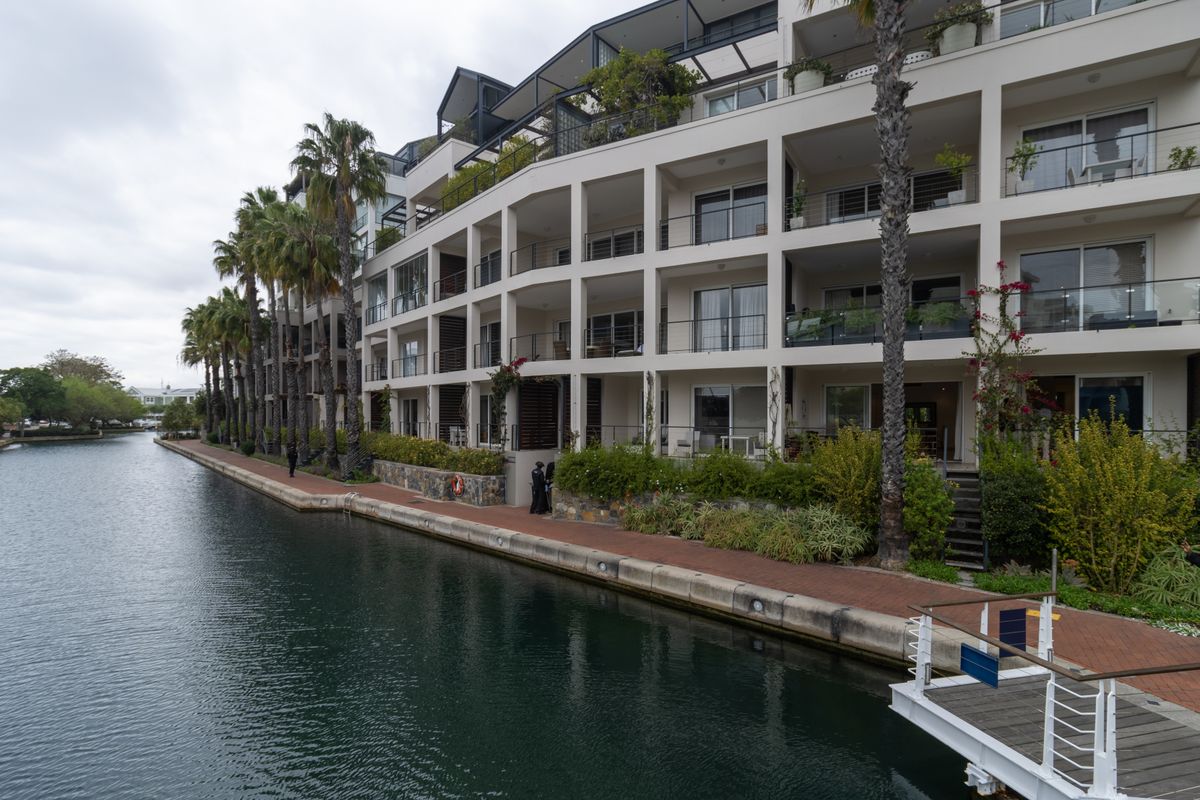 A view of the apartment complex rear facade featuring private balconies, landscaped gardens, and direct access to the canal with a private jetty.